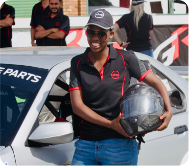 A gentleman holding a helmet smiling next to a race car