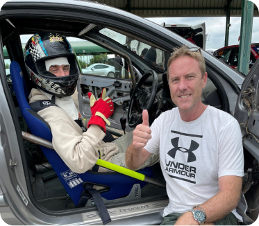 2 people giving thumbs up, with one person in full driving kit, in a racing car